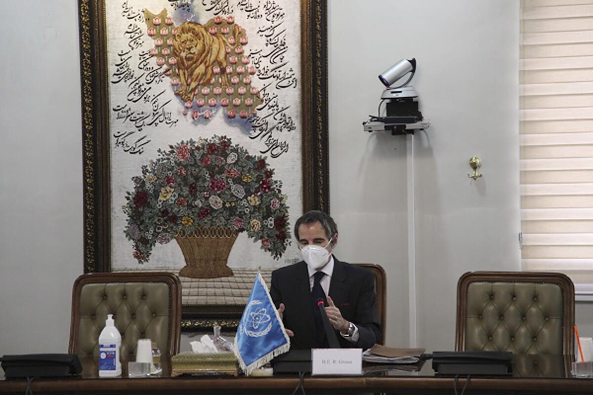 Rafael Mariano Grossi, in surgical mask and seated at a table, gestures as he speaks.