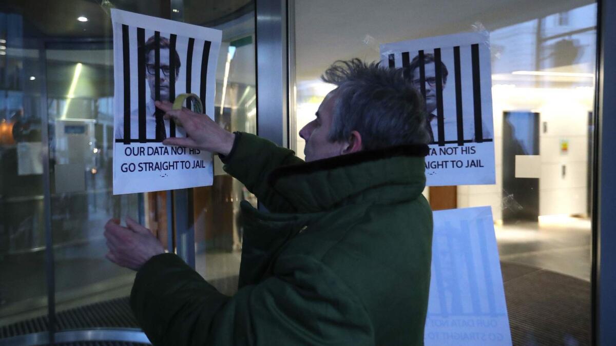 A man affixes posters depicting Cambridge Analytica CEO Alexander Nix behind bars, with the slogan "Our data not his. Go straight to jail" to the entrance of the company's offices in London.