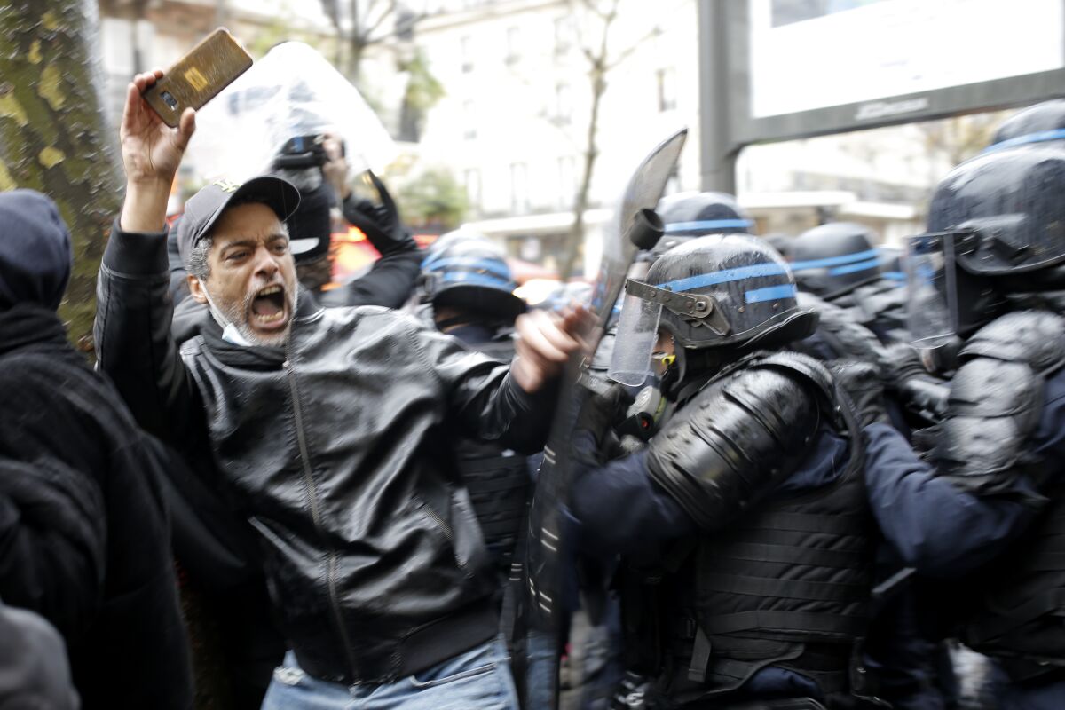 Riot police officers charge a man holding his phone during a protest, Saturday, Dec.12, 2020 in Paris. Protests are planned in France against a proposed bill that could make it more difficult for witnesses to film police officers. (AP Photo/Lewis Joly)