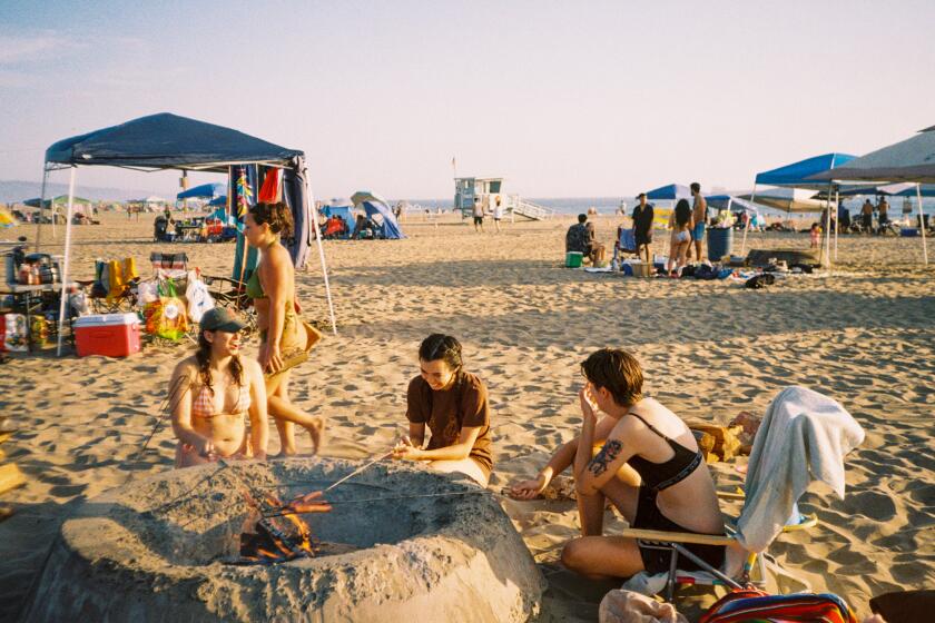 India Shore, Wallice Watanabe and Claire Altendahl roasting hot dogs around a fire pit on Dockweiler Beach.