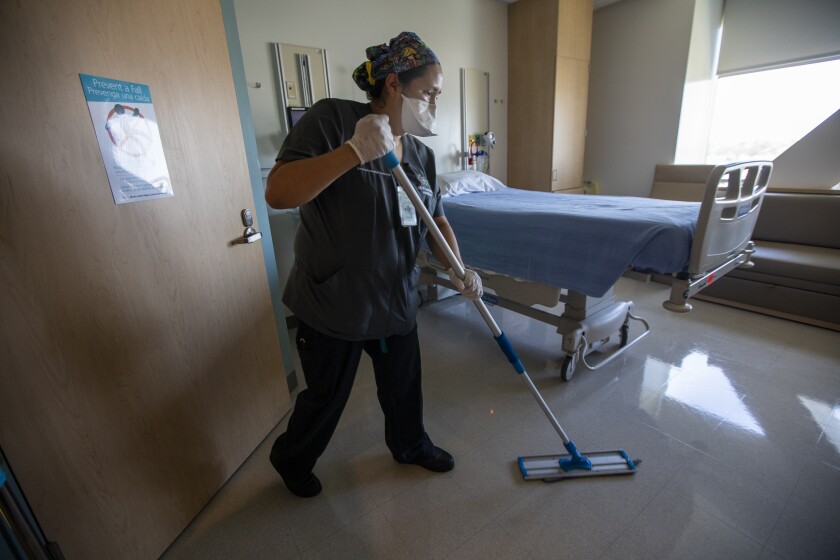 A masked worker mops a hospital room