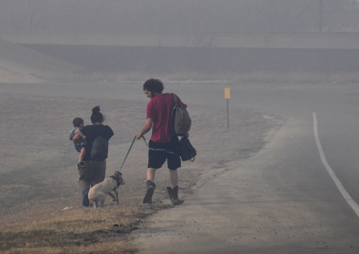 A family walks through smoke down the Arnold Blvd. frontage road after evacuating the Continental Villa mobile home park in Abilene, Texas Thursday March 17, 2022. A quickly-moving grass fire was heading that way, prompting officials to order the evacuation. (Ronald W. Erdrich/The Abilene Reporter-News via AP)