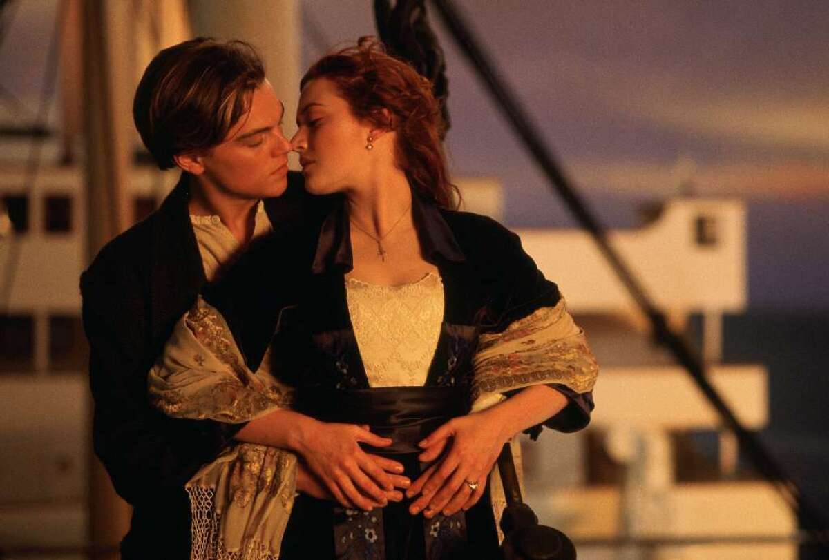 A young man and woman stand at the front of a ship, about to kiss.