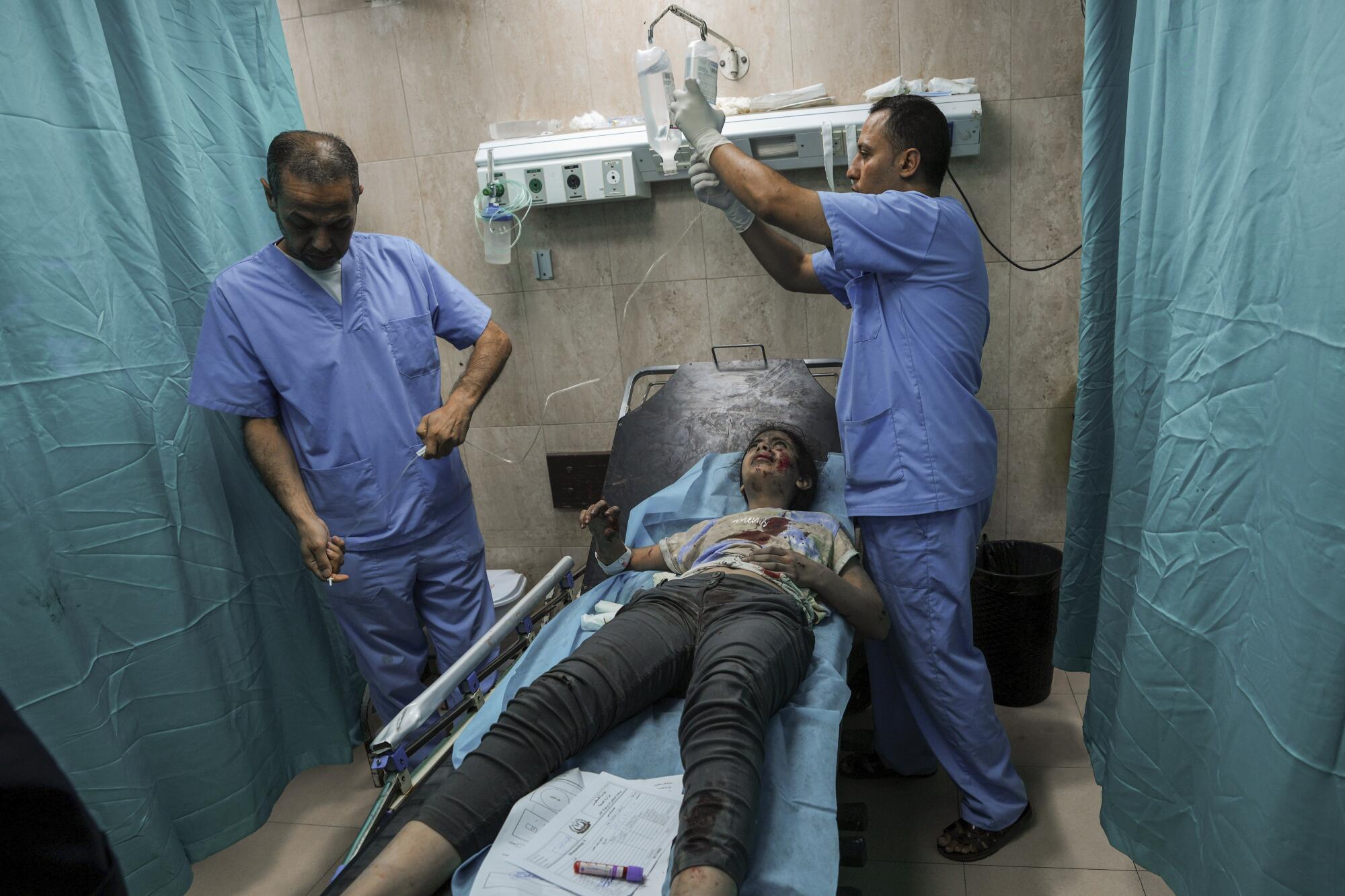 A Palestinian girl lies wounded in a hospital bay as two people give her medical attention. 