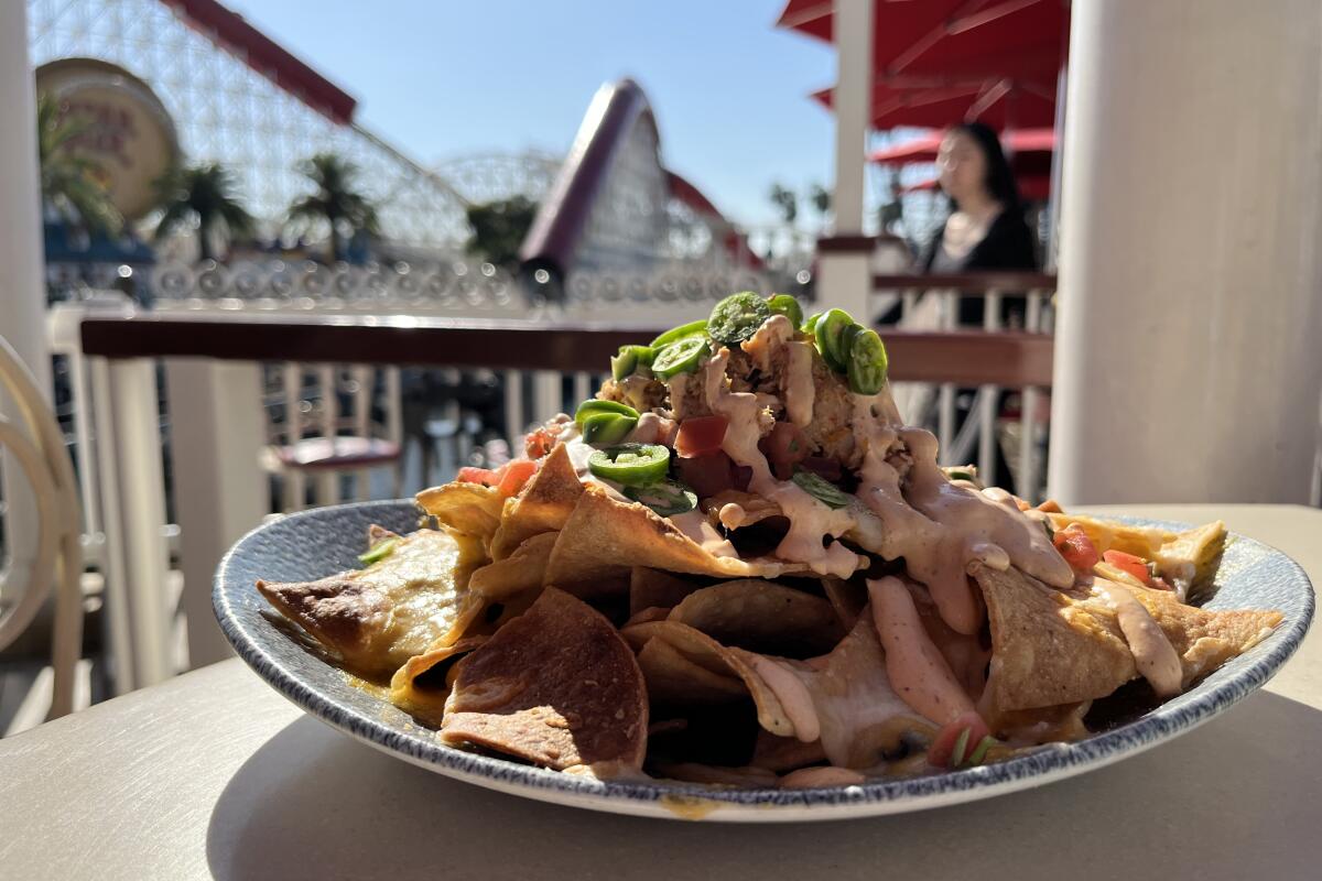 A plate of lobster nachos on an outdoor table, with a roller coaster in the distance