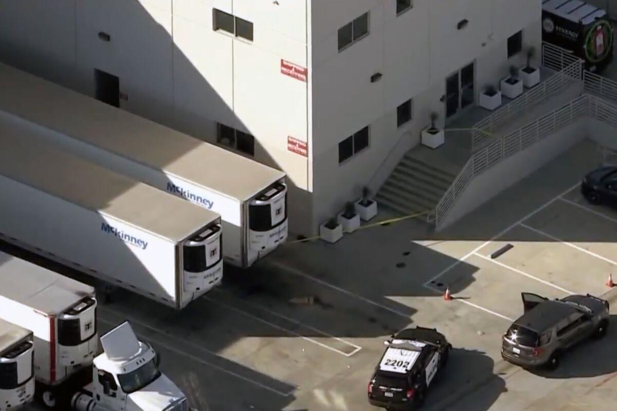 A police car is parked in a lot near a big rig and steps leading into a warehouse.