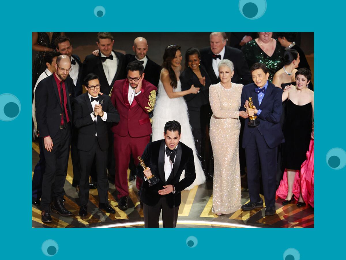 A man in a tux gives an Oscar acceptance speech with his cast and crew behind him