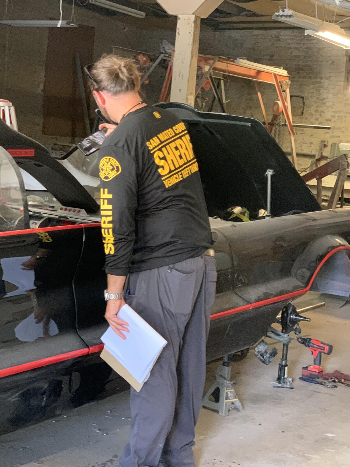 A member of the San Mateo County Sheriff's Department inspects a Batmobile at Fiberglass Freaks.