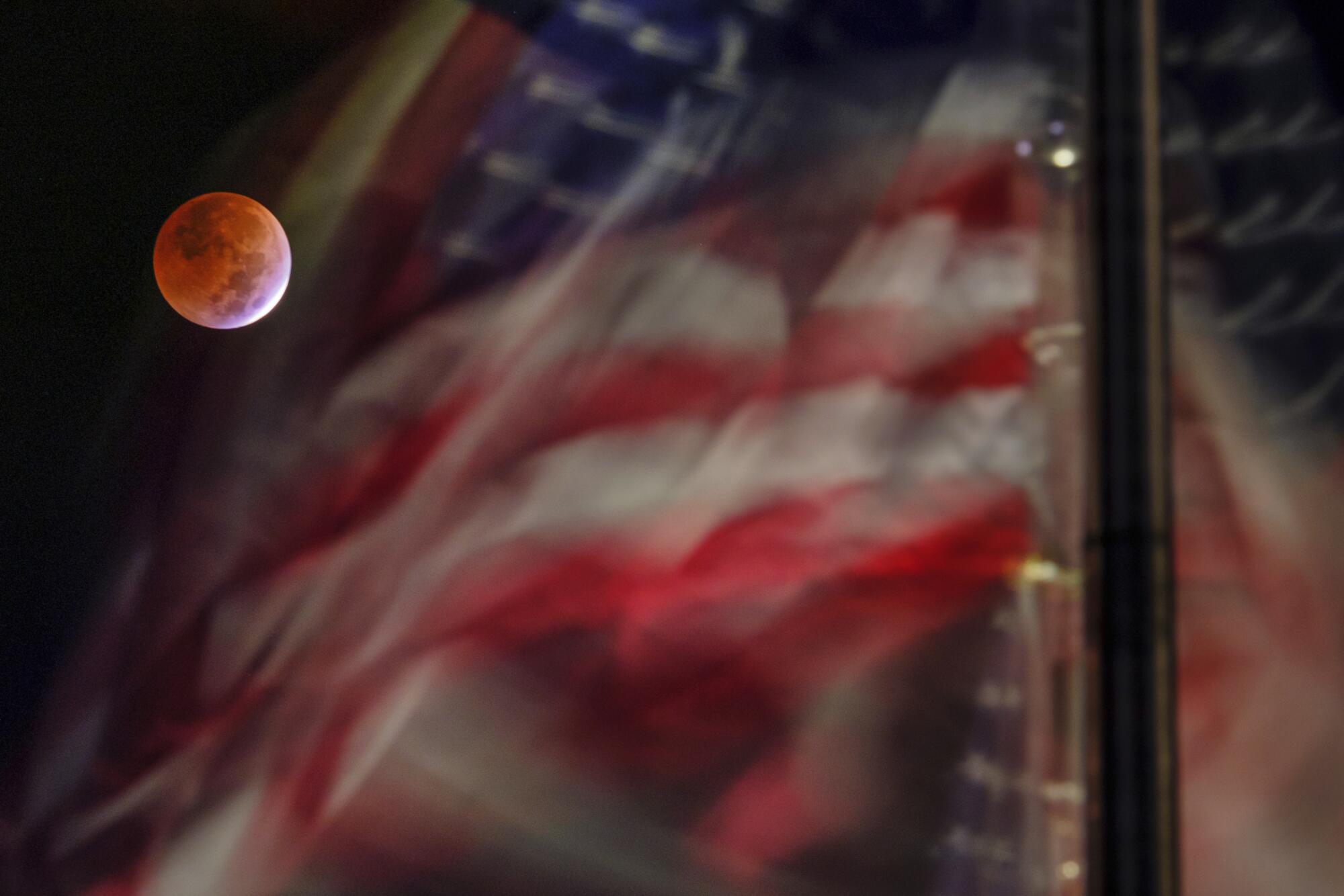 The full blood moon caused by the lunar eclipse is framed by the US Flags blowing in the breeze on the National Mall
