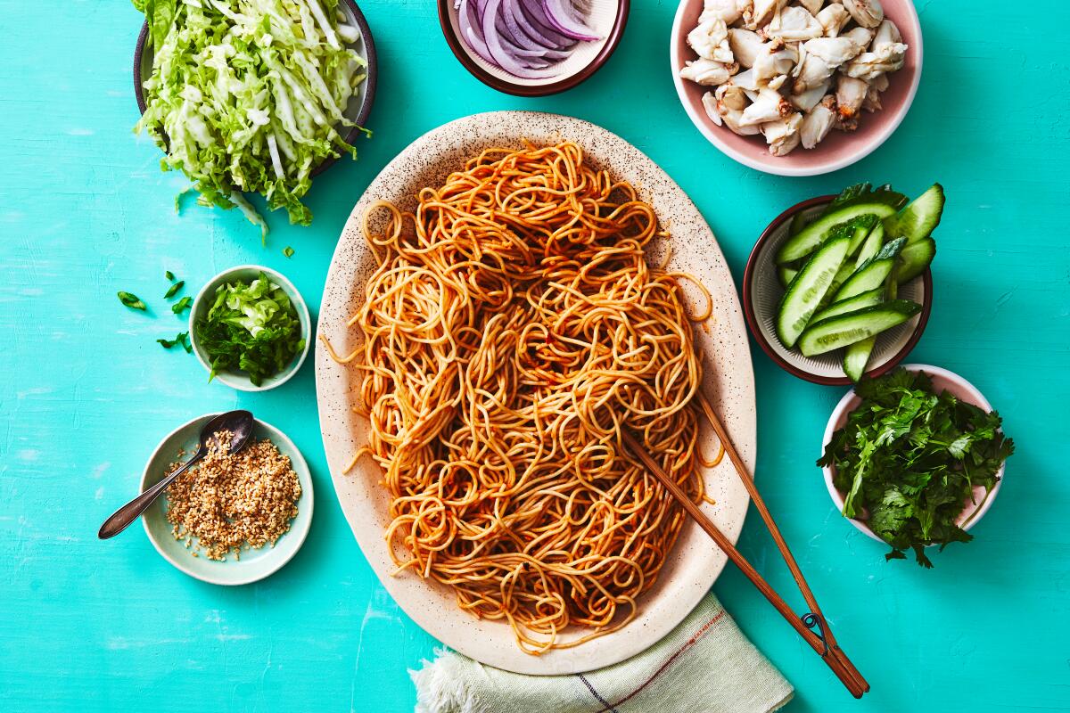 Peanut noodles surrounded by small dishes of crab and vegetables.
