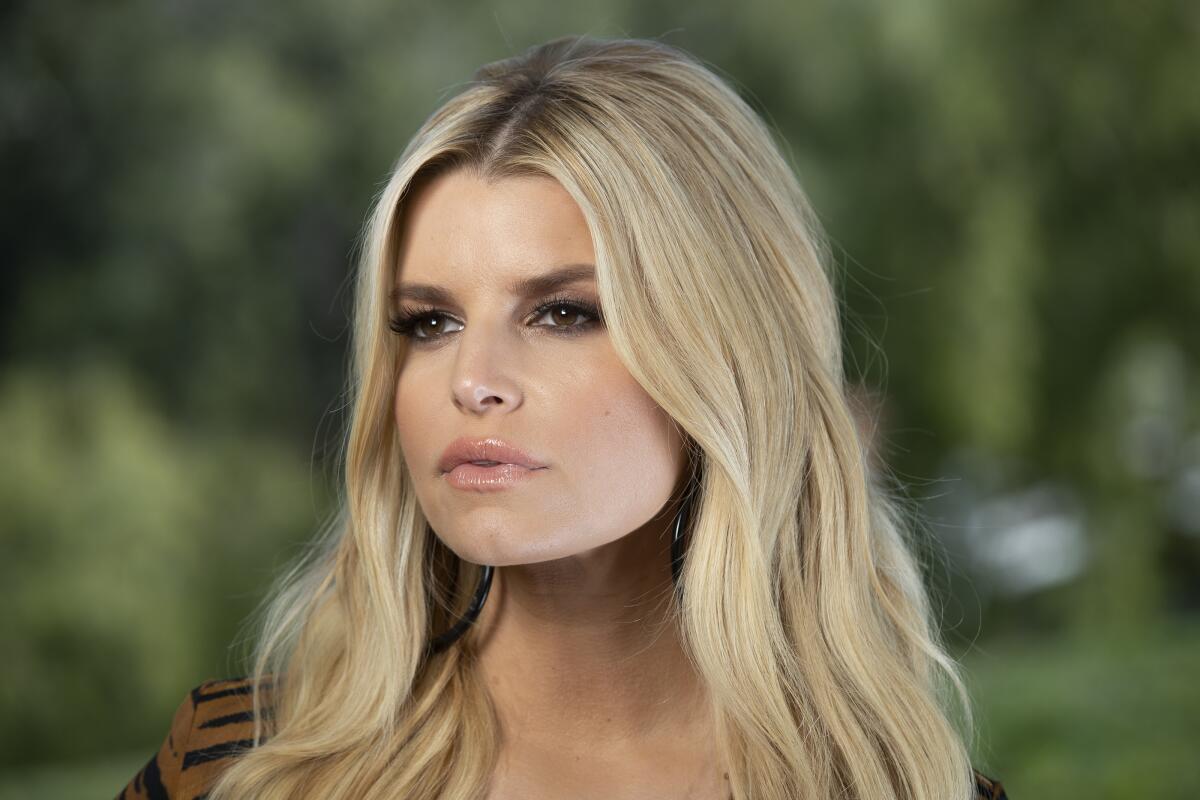 Jessica Simpson looks off camera with a serious expression on her face and blond hair spilling over her shoulders