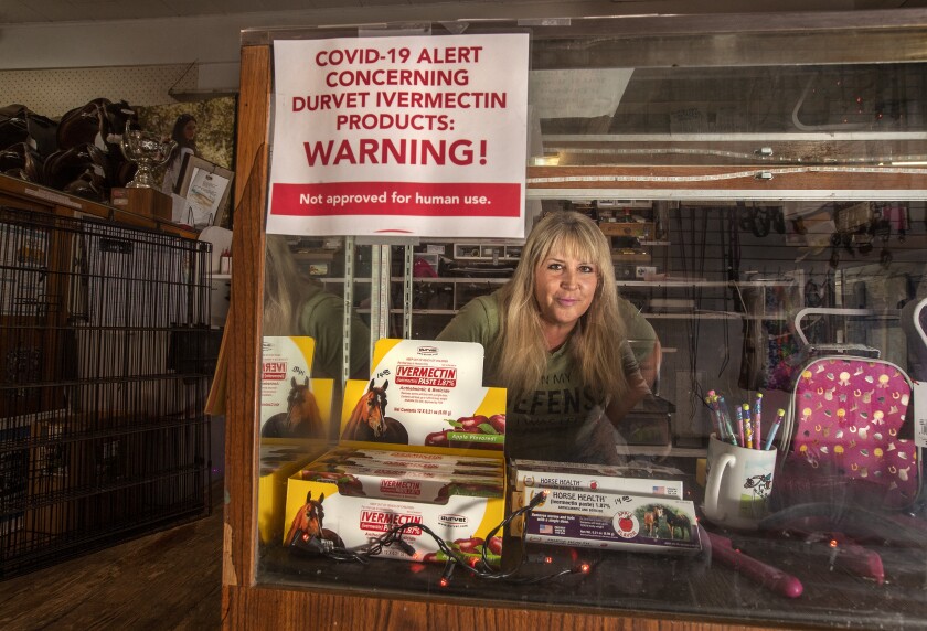 A woman stands behind an ivermectin display with a sign that reads "Warning! Not approved for human use."