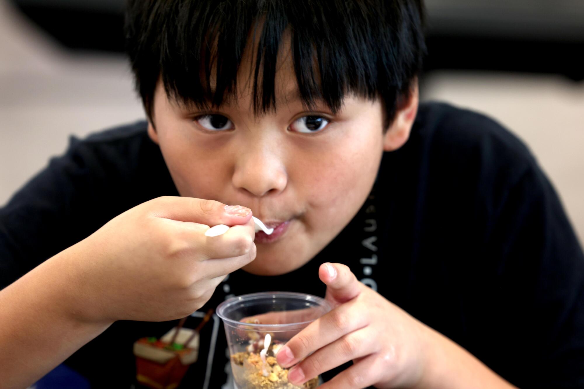 A young boy eats from a cup at at a school meal tasting event. 