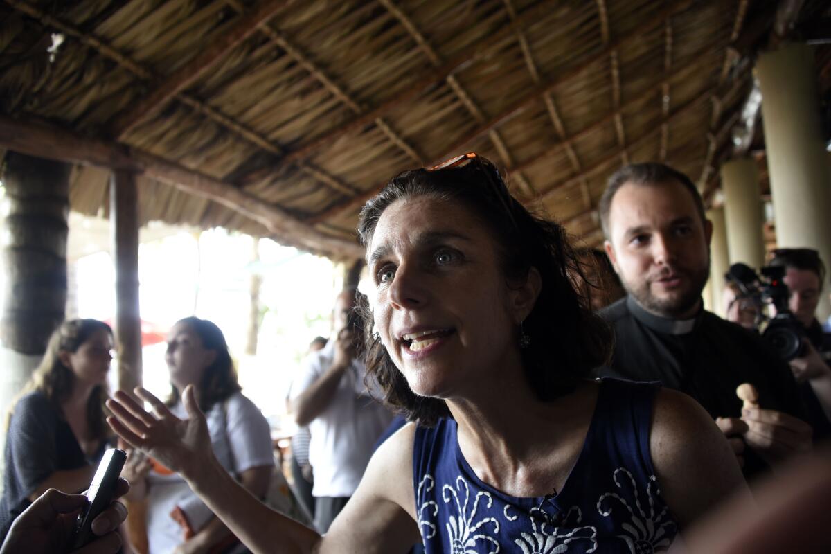 A woman gestures as she speaks as people sit in the background.