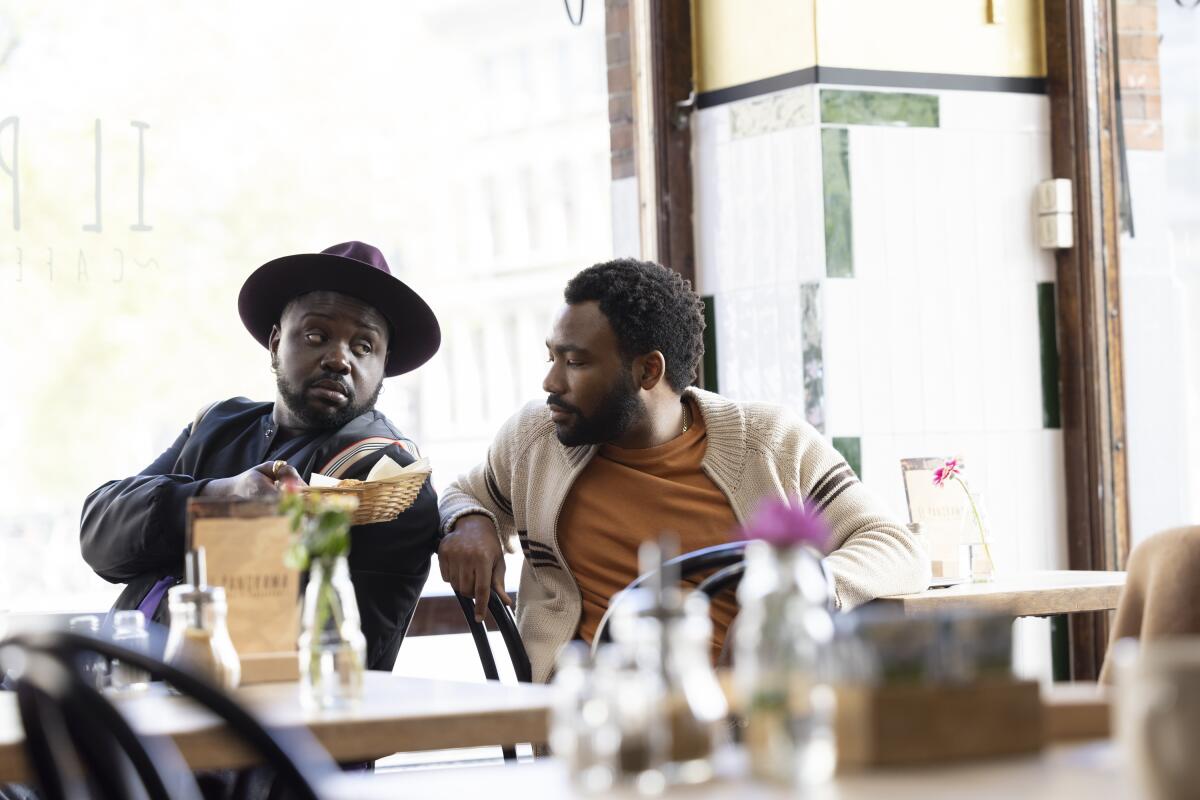 Two men at cafe tables talk together in a scene from "Atlanta."