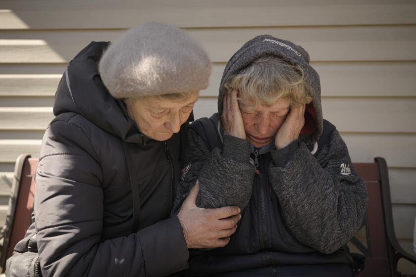 FILE - A neighbor comforts Natalia Vlasenko, whose husband, Pavlo Vlasenko, and grandson, Dmytro Chaplyhin, called Dima, were killed by Russian forces, as she cries in her garden in Bucha, Ukraine, Monday, April 4, 2022. Russian soldiers picked up Dima during a March 4 sweep, accused him of being a spotter helping the Ukrainian military. Asked “What would justice be for you?,” the grandmother of 20-year-old Dima says, “I- I- I can’t even- I don’t know. These scoundrels…” (AP Photo/Vadim Ghirda, File)