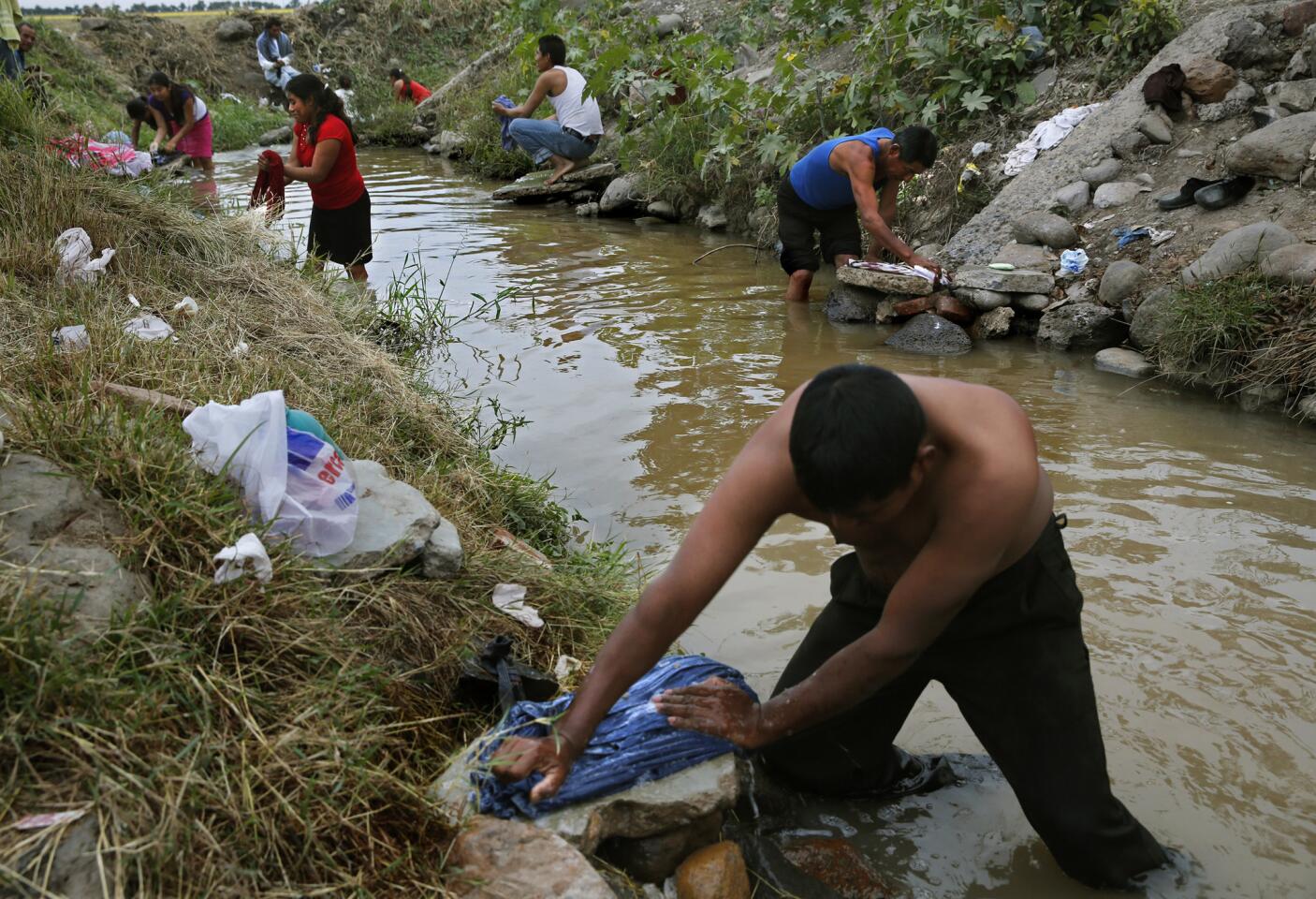 Luis Perez, 26 washes clothes after bathing in an irrigation canal outside Campo San Jose. He says people use the canal because water inside the camp runs out or the pressure is too low in the faucets. Snakes have been known to slither by bathers.