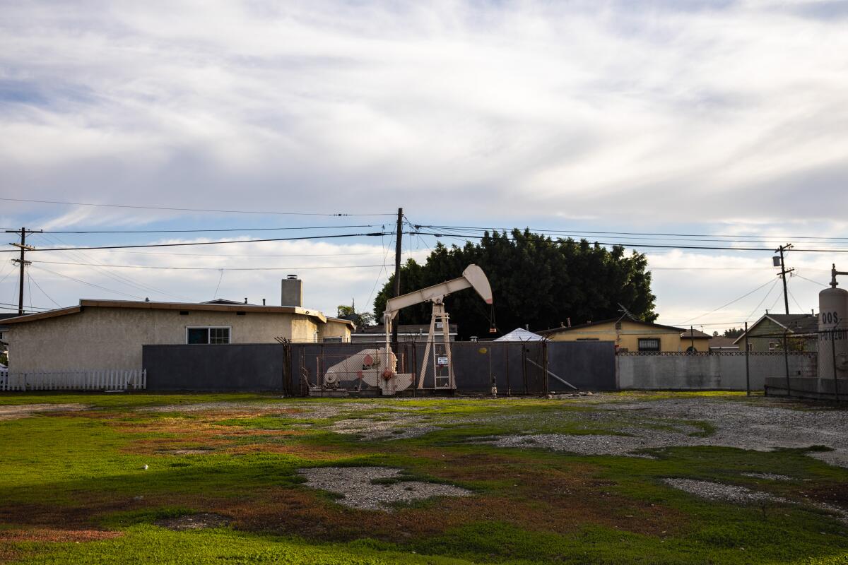  An oil derrick pump is seen on a property, adjacent to homes.