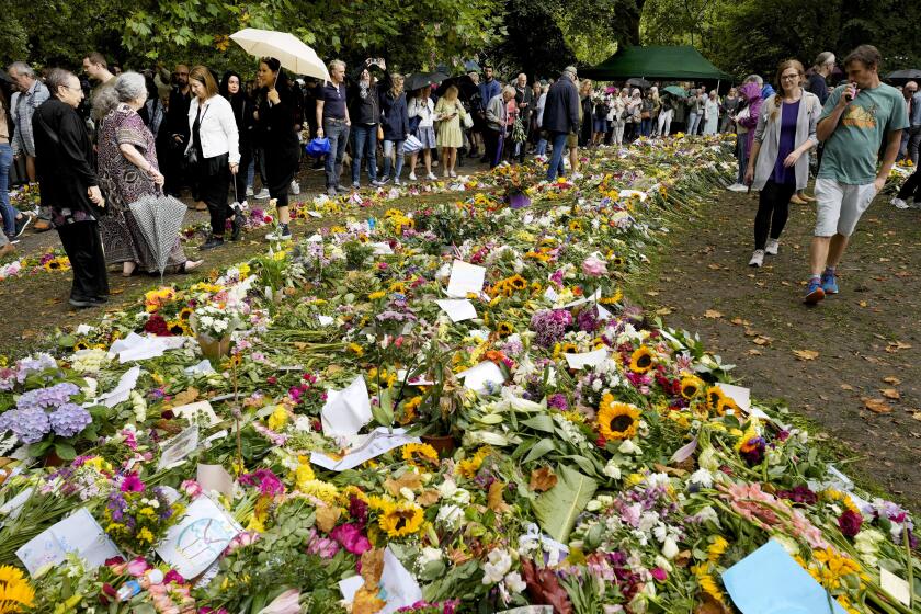 People gather in front of flowers for late Queen Elizabeth II at Green Park, near Buckingham Palace in London, Tuesday, Sept. 13, 2022. Queen Elizabeth II, Britain's longest-reigning monarch and a rock of stability across much of a turbulent century, died Thursday Sept. 8, 2022, after 70 years on the throne. She was 96. (AP Photo/Markus Schreiber)