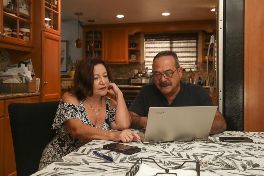 A man and a woman sit at a table and look at a computer screen.