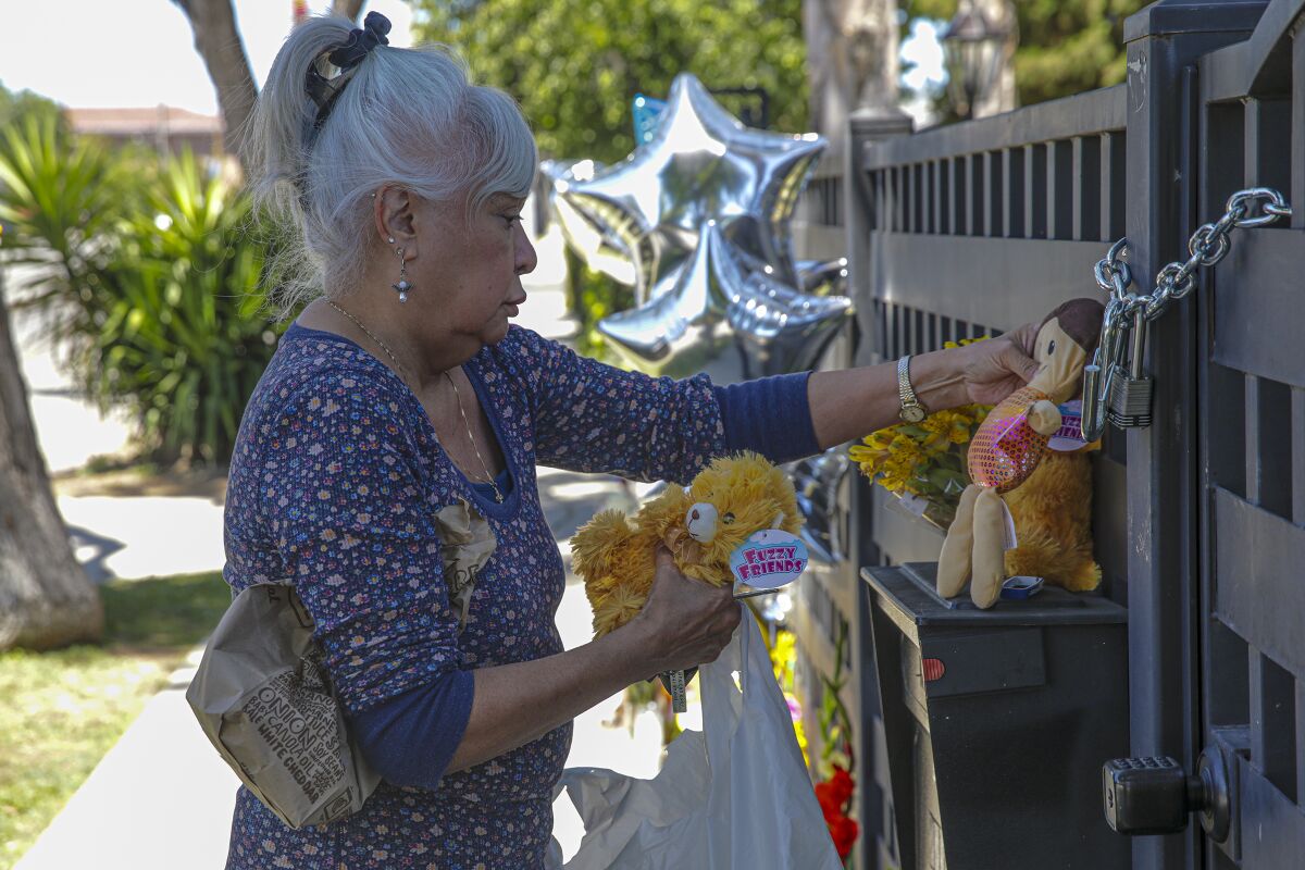 An woman places some stuffed toys at an outdoor memorial