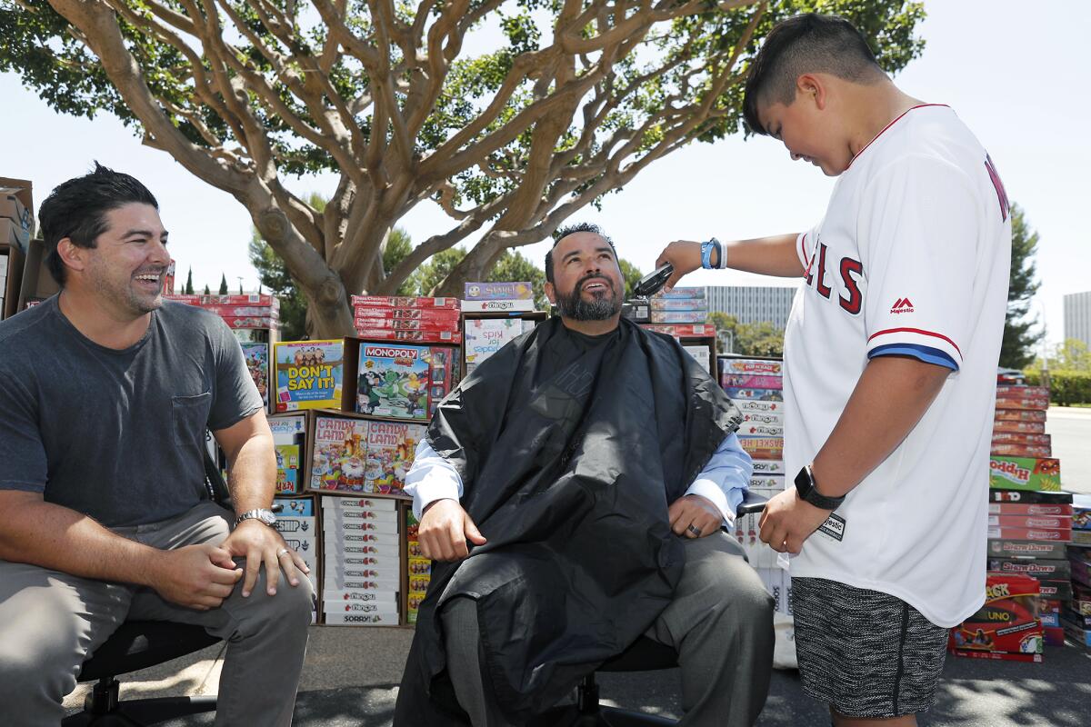 Zachary Maudlin, 13, of Anaheim shaves the beard off Bank of America employee Mike Galvez as Komron Tarkeshian, a vice president at Bank of America in Newport Beach, looks on during an event Friday where bank employees donated nearly 500 board games to Make-A-Wish Orange County and the Inland Empire.