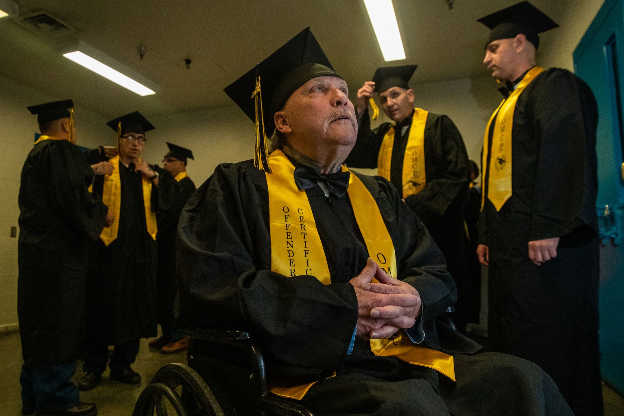 a man in cap, gown, and yellow sash, with others in the same around him