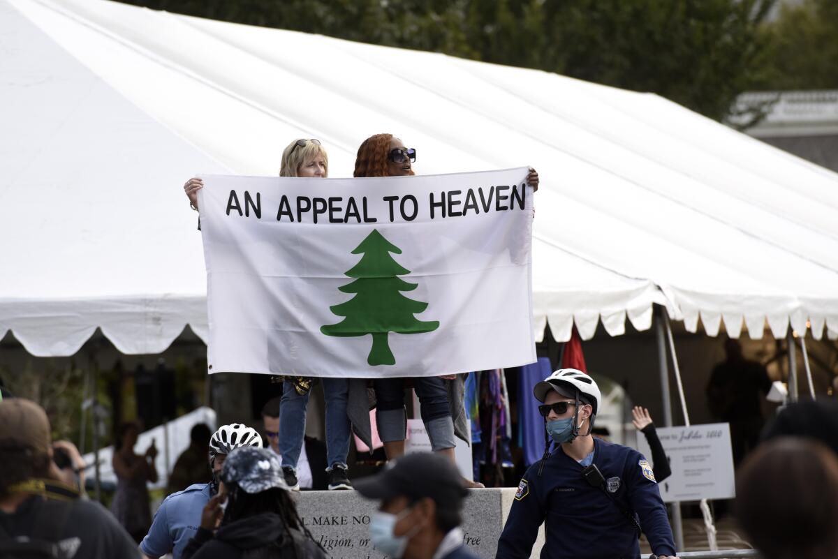 Two people hold up a white batter with a pine tree and the words "Appeal To Heaven."