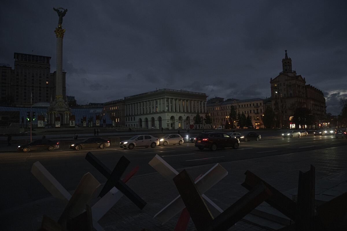 Cars pass darkened buildings and a monument with barricades in the foreground 