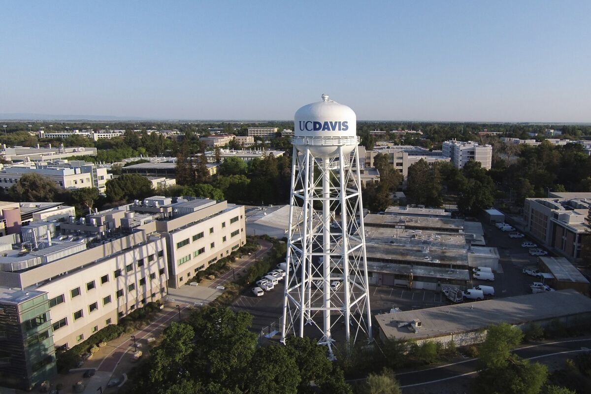 A water tower bearing the UC Davis name rises above campus buildings