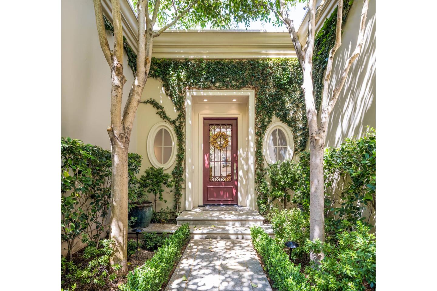 A walkway is tree and shrub lined up to a door.