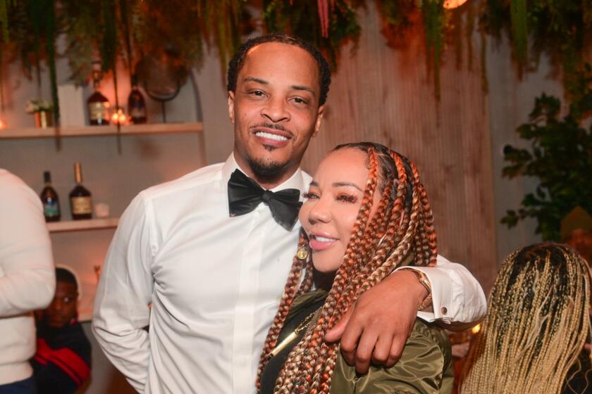 Tip "T.I." Harris in formal wearing with his arm around Tameka Harris with long braids and a olive green bomber jacket