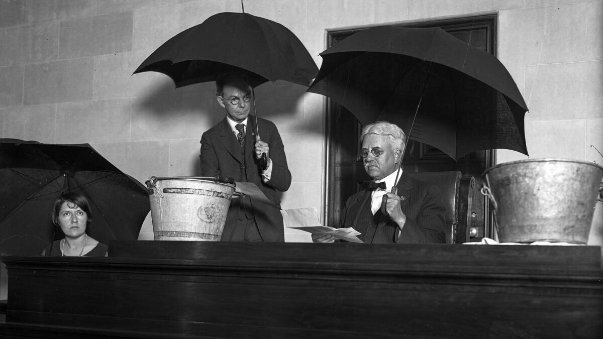 a woman and two men sit under umbrella indoors