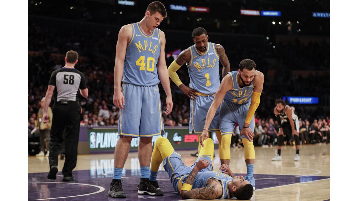 A visibly exhausted Kyle Kuzma is offered a hand by Lakers teammate Tyler Ennis, right, with Kentavious Caldwell-Pope and Ivaca Zubac, after he was fouled on a driving layup against the Spurs in overtime.