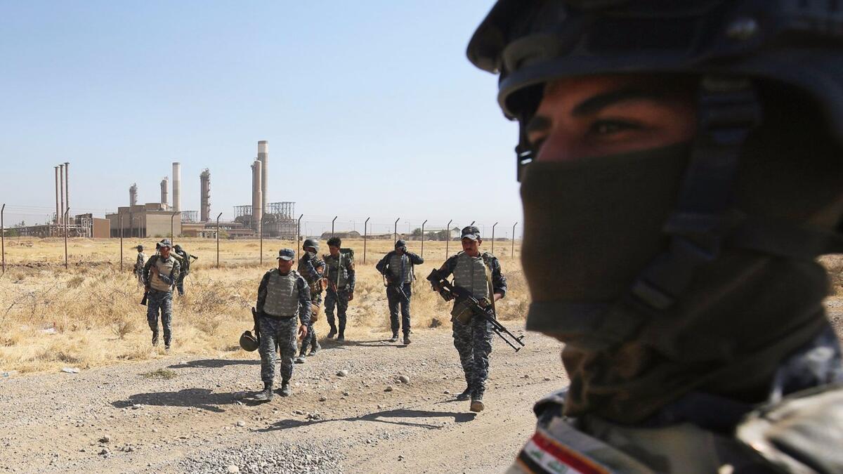 Iraqi government forces pass an oil production plant as they head toward the disputed city of Kirkuk on Monday.