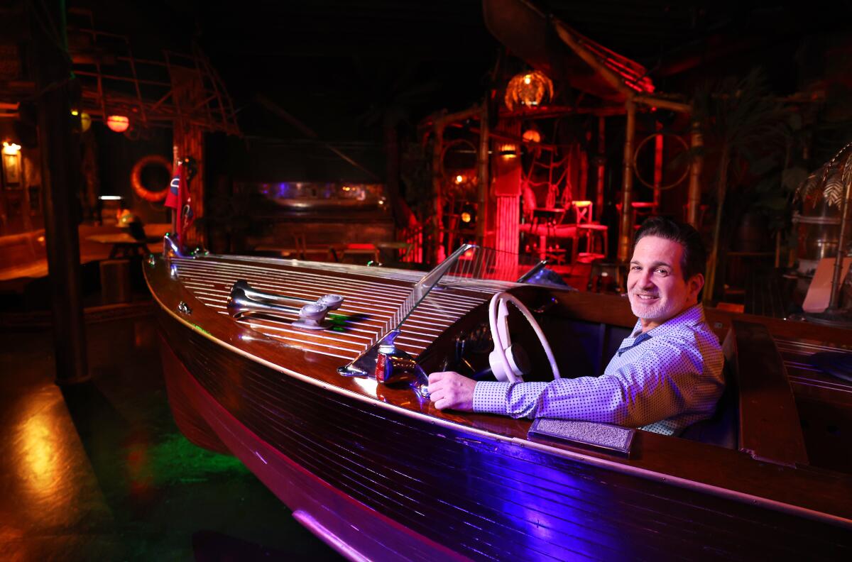 A man in a long-sleeved shirt smiles as he sits in a boat in a dimly lighted restaurant