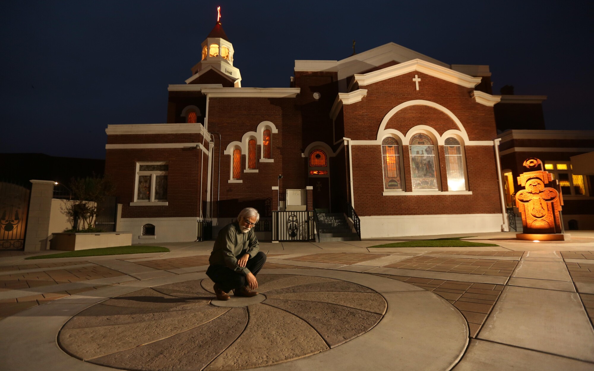 Varoujan Der Simonian kneels in the center of a concrete design outside a church
