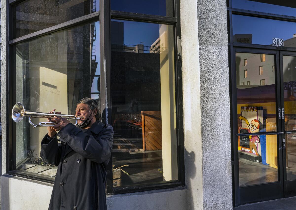 FILE - In this Feb. 5, 2021, file photo, street musician Roberto Hernandez, originally from El Salvador, plays "Lambada" on his trumpet outside Buddy's, a restaurant temporarily closed due to the COVID-19 pandemic, in downtown Los Angeles. Los Angeles County could move into the next phase of reopening with fewer restrictions as early as next week, though any actual lifting of coronavirus-related constraints would not happen immediately, health officials said Wednesday, March 3, 2021. (AP Photo/Damian Dovarganes, File)