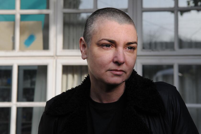 Sinead O'Connor in a dark jacket sitting in front of windows