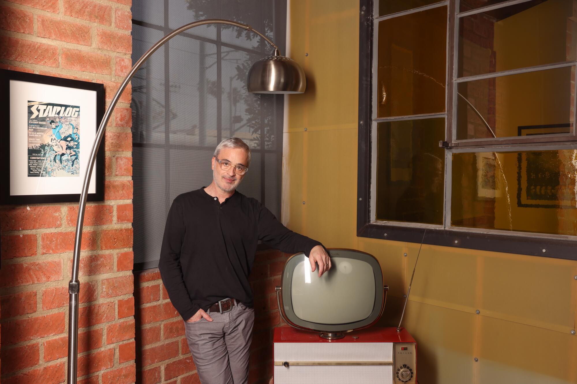 Alex Kurtzman leaning against an old TV set with a lamp hanging above him.