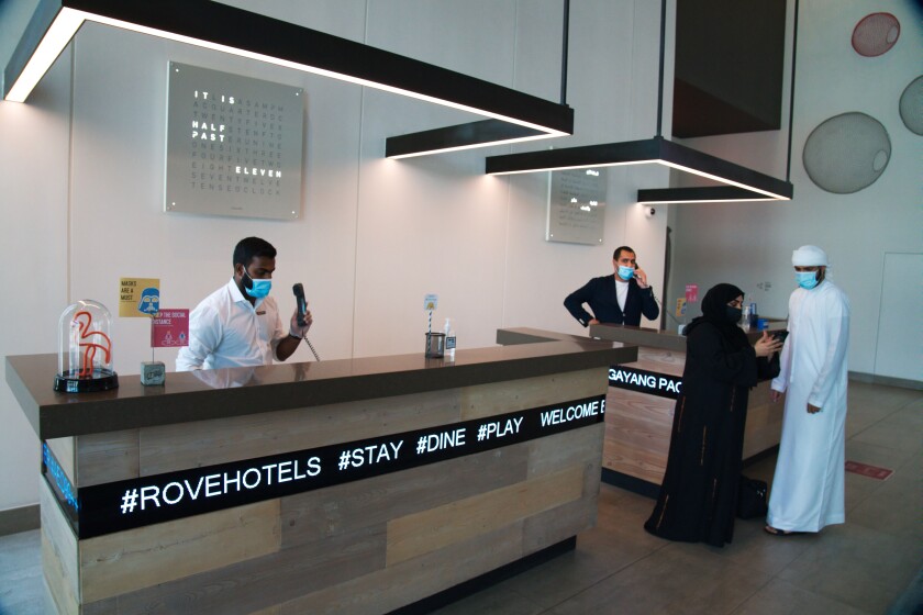 The front desk staff wearing masks due to the coronavirus pandemic help customers at the Rove City Centre Hotel in Dubai, United Arab Emirates, Monday, July 6, 2020. Dubai reopened for tourists Tuesday amid the coronavirus pandemic, hoping to reinvigorate a vital industry for this city-state before its crucial winter tourist season. (AP Photo/Jon Gambrell)