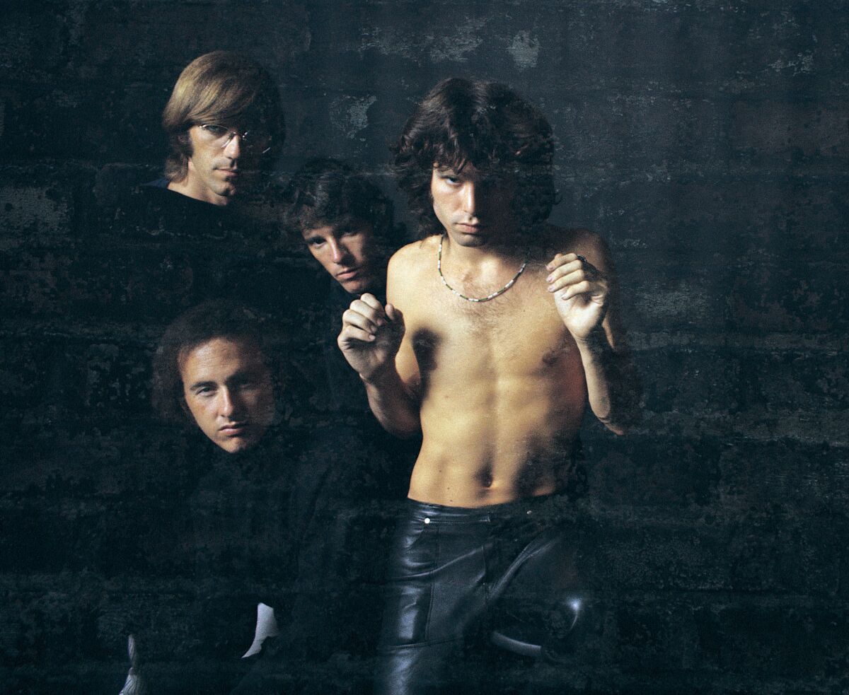 Four men, including a shirtless Jim Morrison, in front of a black background.