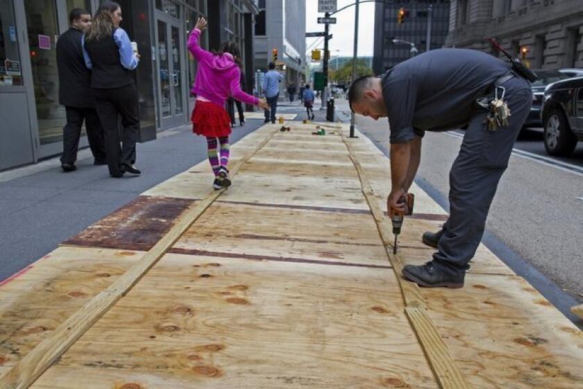 A worker puts plywood over sidewalk grates in Lower Manhattan as Wall Street prepares for Hurricane Sandy.