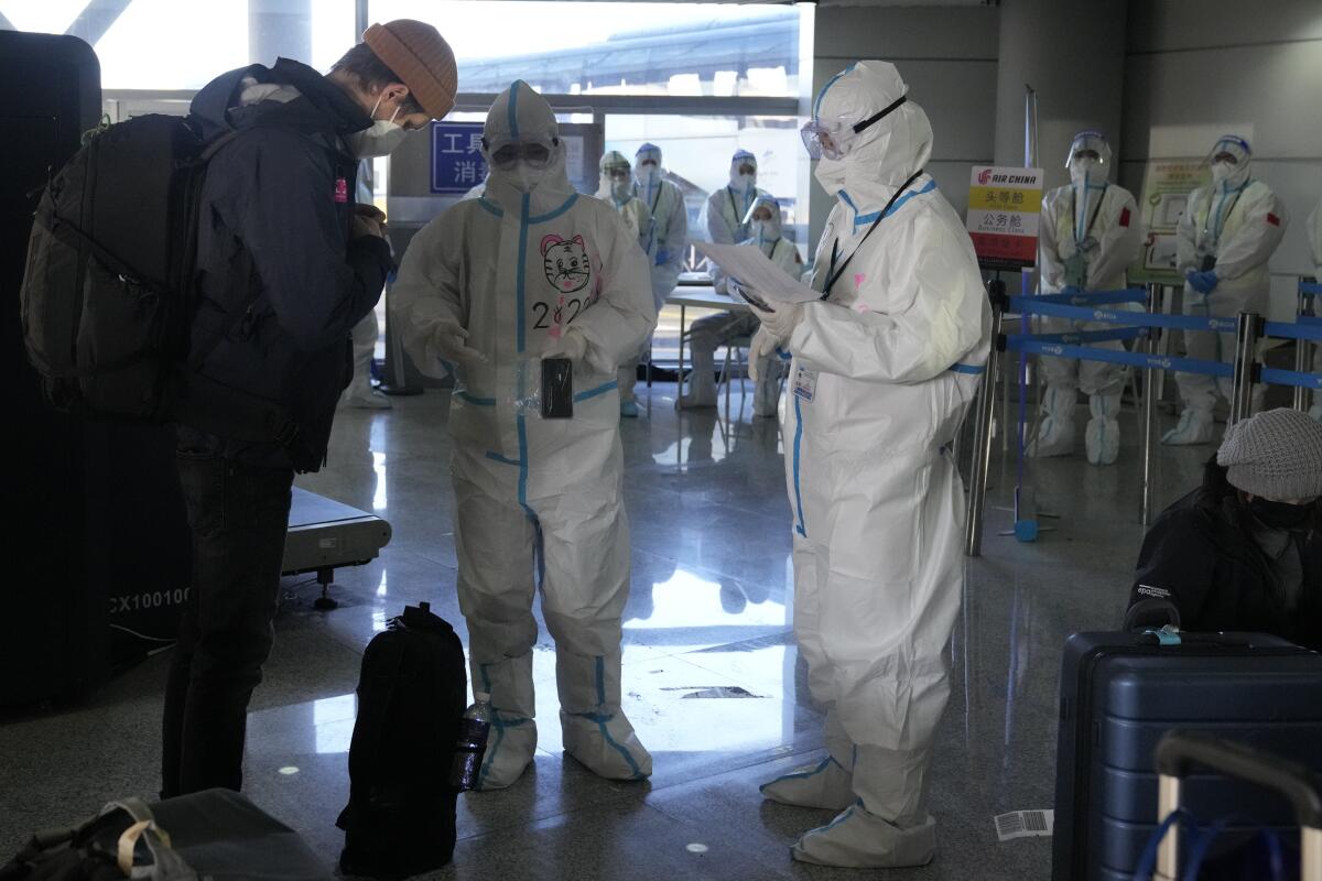 Workers wearing protective suits at the airport assist guests ahead of the 2022 Winter Olympics.