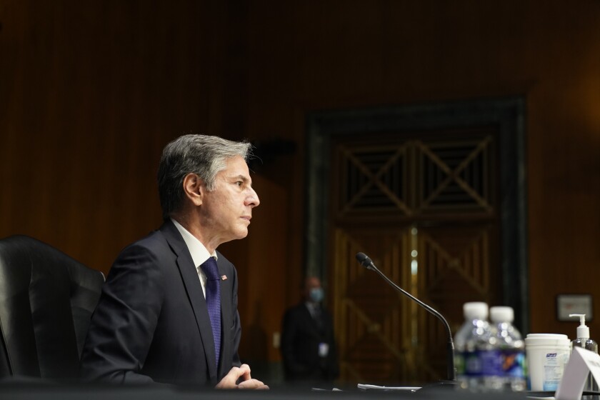 Secretary of State Antony Blinken sits in a chair in a paneled room.