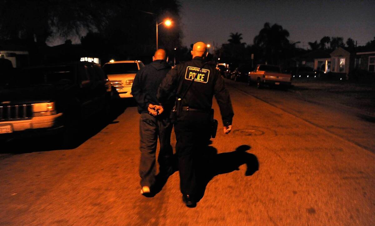 A man is escorted to a vehicle after being arrested by a Department of Justice law enforcement officer in Whittier on suspicion of illegally possessing a handgun.