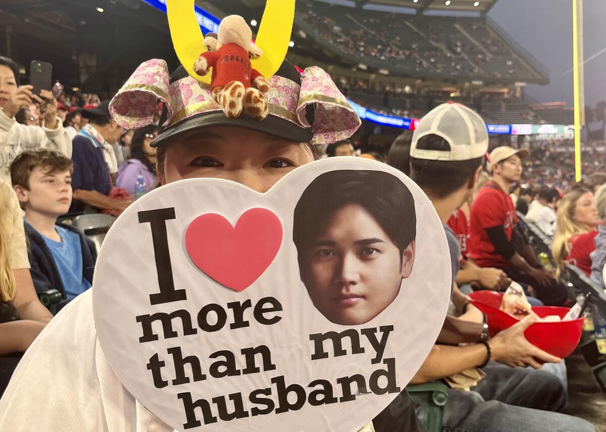 Mika Shimura sits in the stands at Angel Stadium holding a "I love Shohei Ohtani more than my husband" sign.