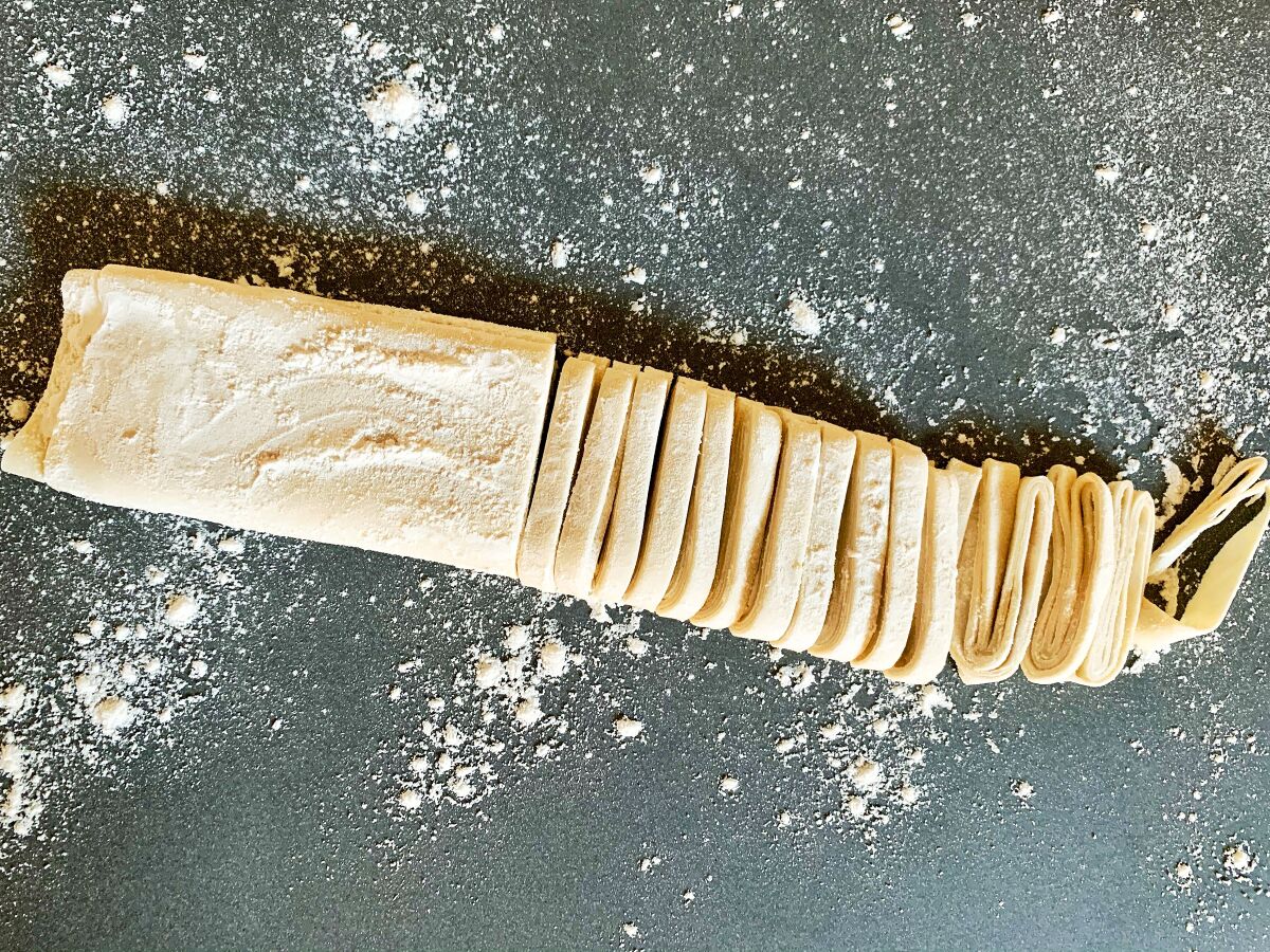 A long rectangle of dough, half of which has been cut into noodles