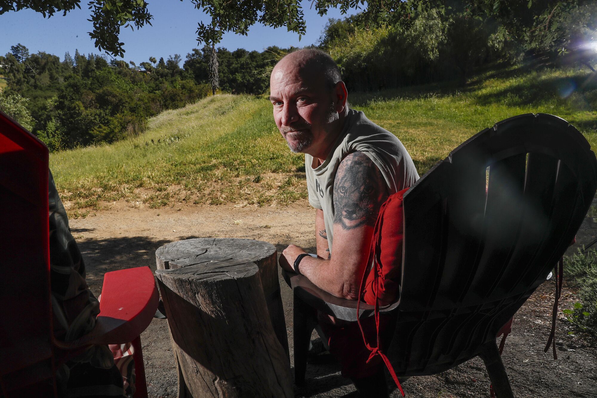 A man sitting outside turns in his chair, revealing a large tattoo of a mountain lion's face covering his left shoulder