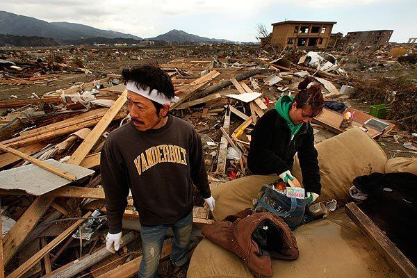 Kamihachi, Japan -- Meguni Sasaki, right, and her husband Satoru Sasaki, both 36, return to their neighborhood to collect what few possessions they can find after the devastating earthquake and tsunami. One of the items was a couch. "This used to be in our living room," said Meguni Sasaki. "It was so expensive." Satoru located the second floor of their home about a quarter of a mile away from its original location, where they also found a couch and a few possessions.